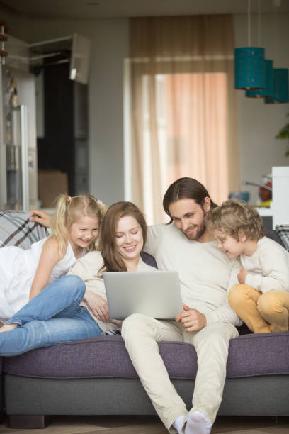 istock Family with children having fun using laptop on sofa, vertical 874986430