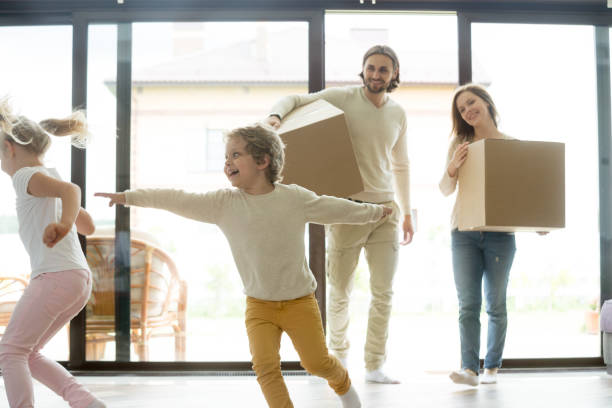 istock Kids playing in new home, parents holding boxes, moving day 874986472
