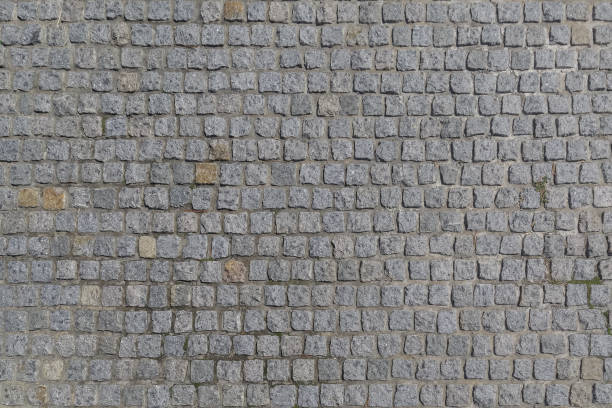 a estrada é pavimentada com pedras de granito, de uma forma quadrada como um fundo ou um pano de fundo - paving stone cobblestone road old - fotografias e filmes do acervo