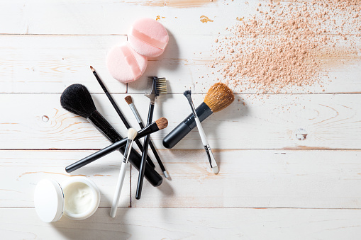 Concept of cosmetics and makeup with free powder, skincare and various professional make up face brushes over white wooden background for elegant beauty background, flat lay view
