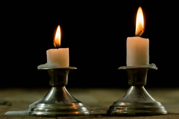 candles burning in candlesticks on a wooden table. Silver candlesticks. Black background