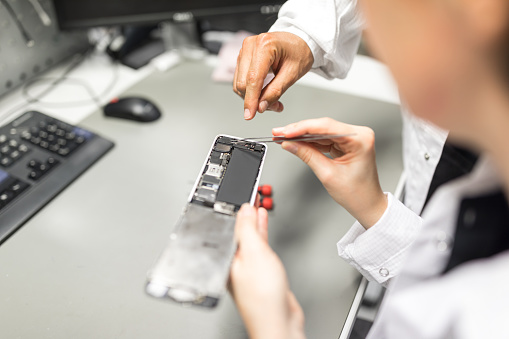 Close up of female technician hands fixing a smart phone with guidance from  male colleague. Technician learning repairing a mobile phone in service center from coworker,