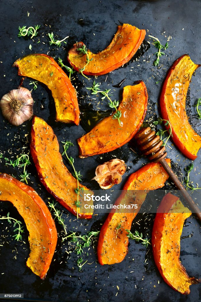 Oven baked pumpkin slices Oven baked pumpkin slices with garlic and thyme served with honey on a black metal tray.Top view. Roasted Stock Photo