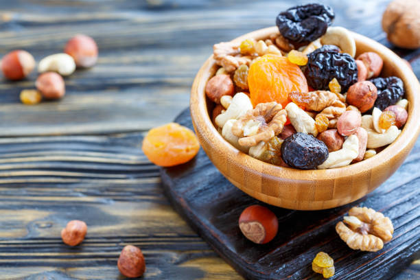 Nuts and dried fruit in a wooden bowl. Bowl with a mixture of dried fruit and nuts on an old kitchen table, selective focus. dried fruit stock pictures, royalty-free photos & images