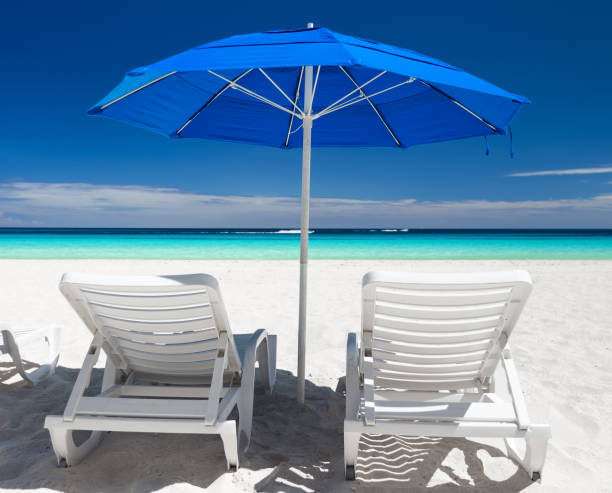 istock Caribbean beach with blue sun umbrellas and white beds 875024234