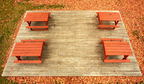 Pole aerial High Dynamic Range (HDR) image of four picnic tables on a wooden platform surrounded by autumn leaves and grass.