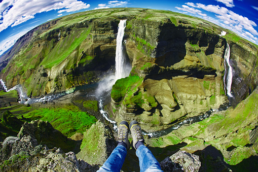 famous Haifoss waterfall in southern Iceland. treking in Iceland. hiker makes selfi by photographing his legs from above. A man is sitting on the edge of a cliff