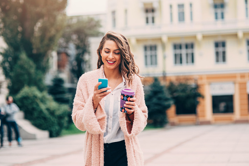 Woman using a smart phone and drinking coffee in the city.