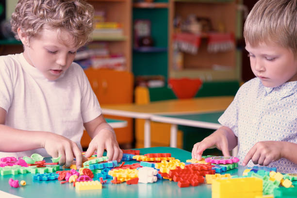 istock Cute caucasian boy in a white shirt playing with colorful constructor details. Activities with children in kindergarten. 875054320