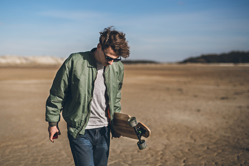 Young rebelious skater with his board, walking alone