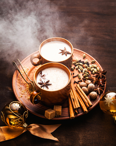 reeky Masala tea chai latte traditional hot Indian teatime ceremony sweet milk with spices, herbs organic infusion healthy beverage in porcelain cup on wooden table background. Christmas style. New Year's decorations