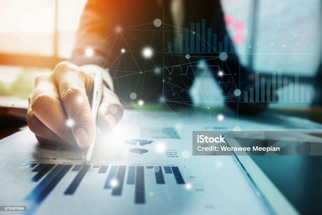 Close up Businessman hand holding pen and pointing at financial paperwork with financial network diagram. Finance Stock Photo