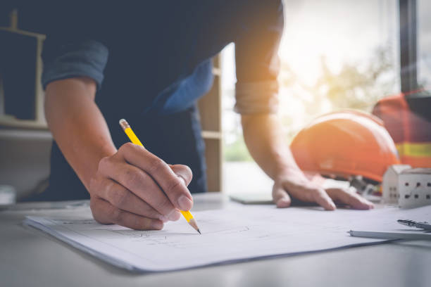 istock Architect man holding pencil working with laptop and blueprints for architectural plan, engineer sketching a construction project concept. 875088138