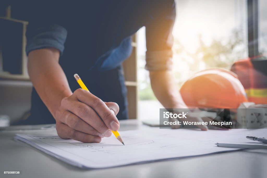 Architect man holding pencil working with laptop and blueprints for architectural plan, engineer sketching a construction project concept. Plan - Document Stock Photo