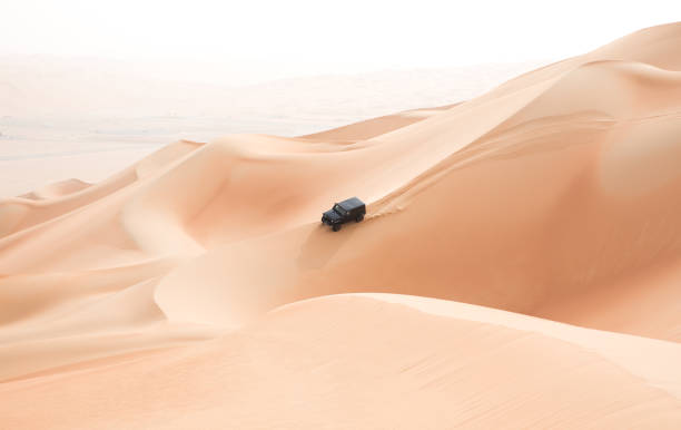 A single black car scaling giant dunes in the Empty Quarter desert. Abu Dhabi, UAE - Jul 21, 2017: A single black car scaling giant sand dunes in the Empty Quarter desert on a very bring and hazy summer morning sunrise. kite sailing stock pictures, royalty-free photos & images