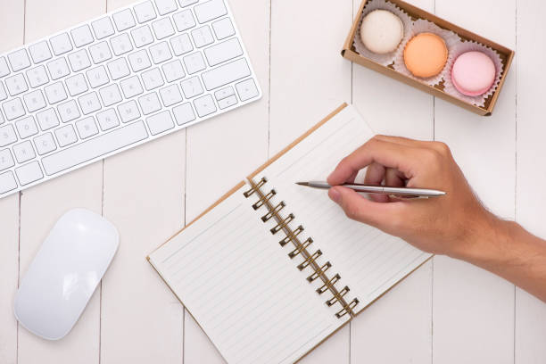 istock Man writing on open notebook on white desk with colorful macaroons, keyboard. 875096808