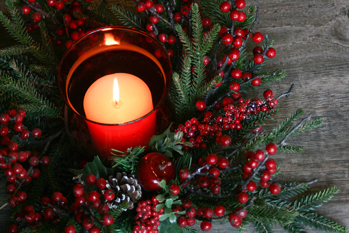 Candle decorated with peaces of Christmas tree, light and ornaments. White Candles and little ceramic houses.