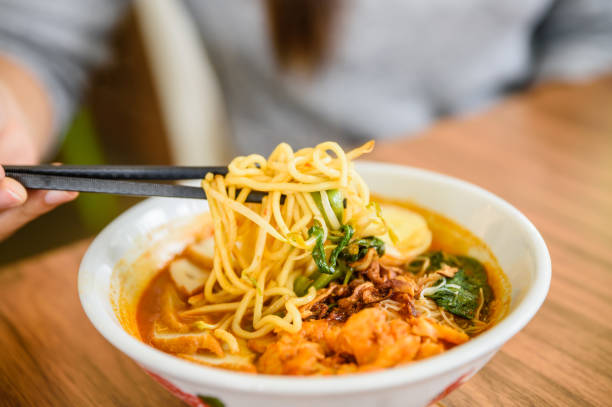 mano con bacchette cinesi che mangiano noodle, una famosa zuppa di noodle cerry di gamberi malesi. - hokkien foto e immagini stock