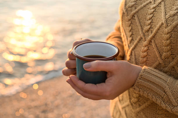 cozy autumn by the sea. female hands holding a mug with tea - sky human hand water white imagens e fotografias de stock