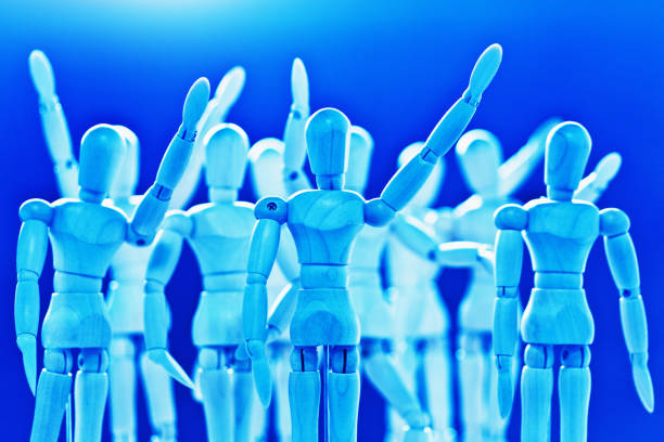 A group of wooden lay figures, brightly lit and blue-toned, waves at something or someone in greeting or farewell.
