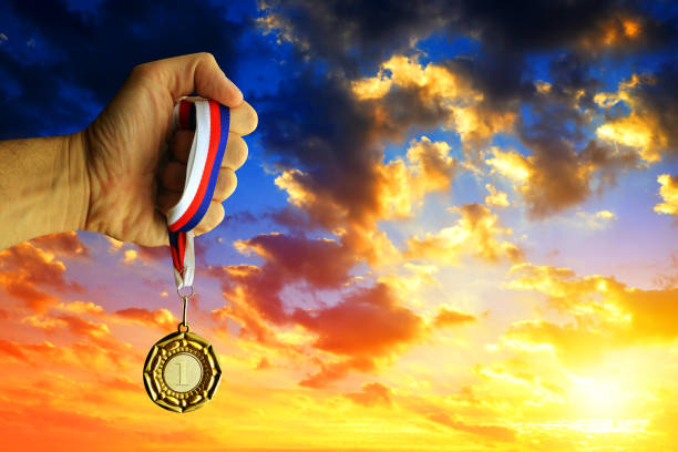 Hand holding a golden medal against sunset sky.