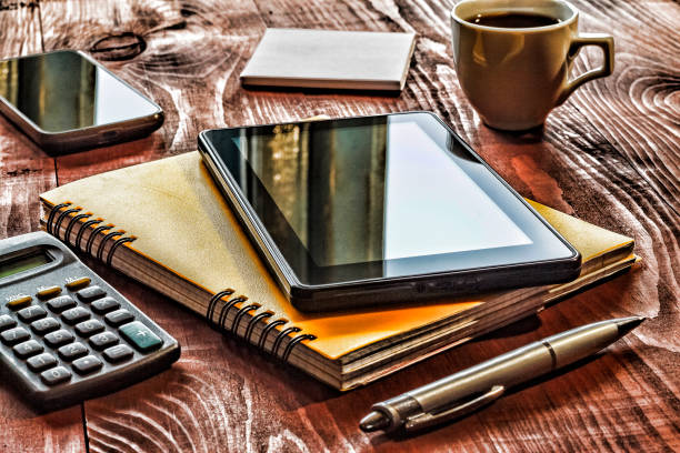 Over the shoulder view of hand taking notes on a table with a digital tablet and cup of coffee.  Minimal working place concept.