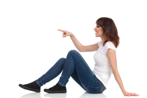 istock Smiling Young Woman Is Sitting On Floor, Pointing And Looking Away. Side View 875172594