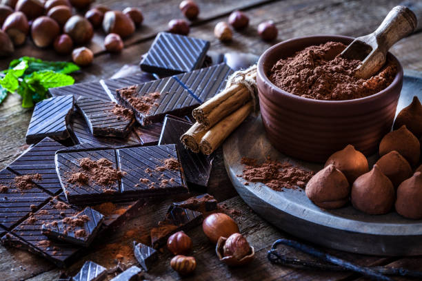 Preparing homemade chocolate truffles Rustic wooden table filled with ingredient for preparing homemade chocolate truffles. The composition includes dark chocolate truffles, chocolate bars, cocoa powder, cinnamon sticks, vanilla beans, mint leaves and hazelnuts. Predominant color is brown. cacao fruit stock pictures, royalty-free photos & images