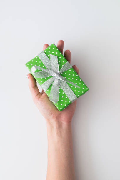 istock Woman hand holding green gift box isolated on white background. Top view, flat lay. Copyspace. 875182992