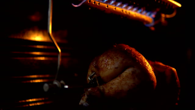 The bird on a spit turns and is fried under a gas burner in the oven.