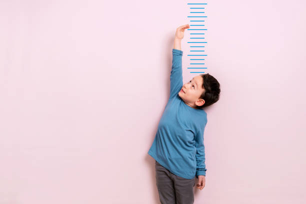 Child measuring his height Child measuring his height on wall. He is growing up so fast. one boy only stock pictures, royalty-free photos & images