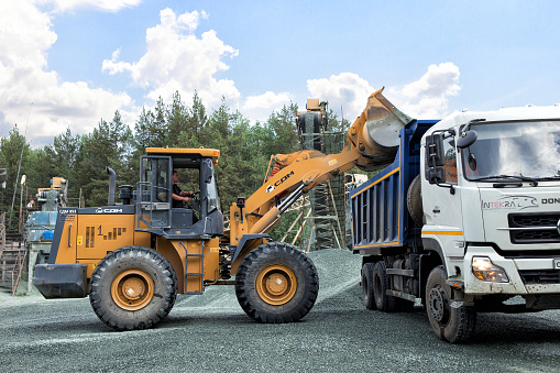 Ekaterinburg, Russia - June 06, 2017: Construction equipment and machinery, a pile of construction gravel, yellow digger loads crushed stone into dumper truck tipper