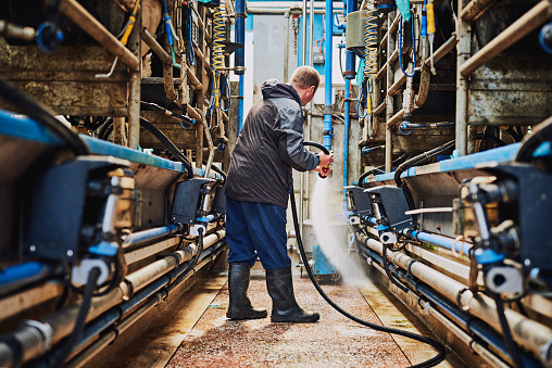 Full length shot of a male farmer hosing off the floor inside a dairy factory