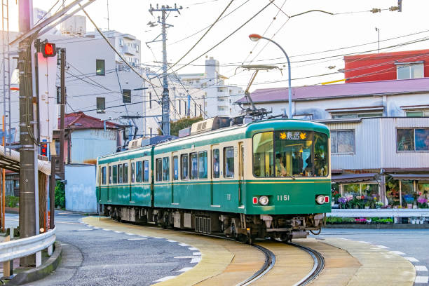 Enoshima Electric Railway (Enoden) street-running in Kamakura City, Japan Fujisawa, Japan – October 26, 2017:  Enoden electric train departing Enoshima station and running down middle of Katasekaigan street in Kamakura City, Kanagawa, Japan.  The Enoshima Electric Railway (Enoden) is a 100yo private railway connecting the cities of Fujisawa and Kamakura with 10km or 6 miles of 1067mm single track with passing loops. Power is 600V DC. sagami bay photos stock pictures, royalty-free photos & images