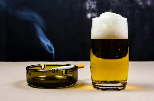 Beer with high foam in a pint and a cigarette on an ashtray.