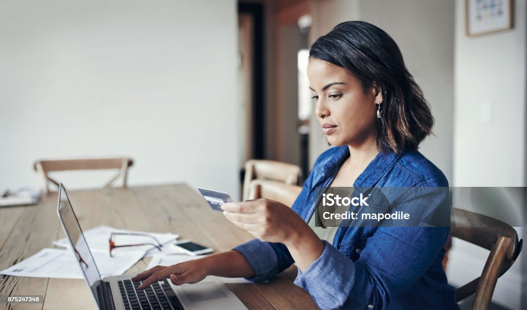 Making banking transactions from the comfort of home Shot of a young woman using a laptop and credit card while working from home Credit Card Stock Photo