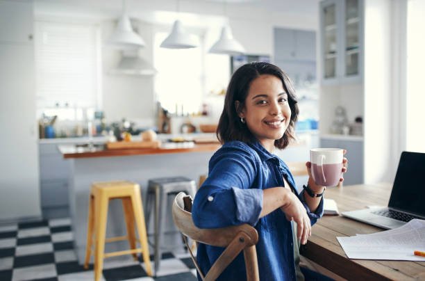 Taking care of business with a cuppa tea Shot of a young woman having a coffee break while working from home looking over shoulder stock pictures, royalty-free photos & images