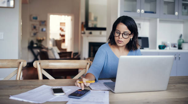 What's the budget looking like this month? Shot of a young woman using a laptop and calculator while working from home financial bill stock pictures, royalty-free photos & images