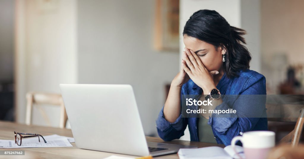 When working from home isn’t work out Shot of a young woman looking stressed while using a laptop to work from home Emotional Stress Stock Photo