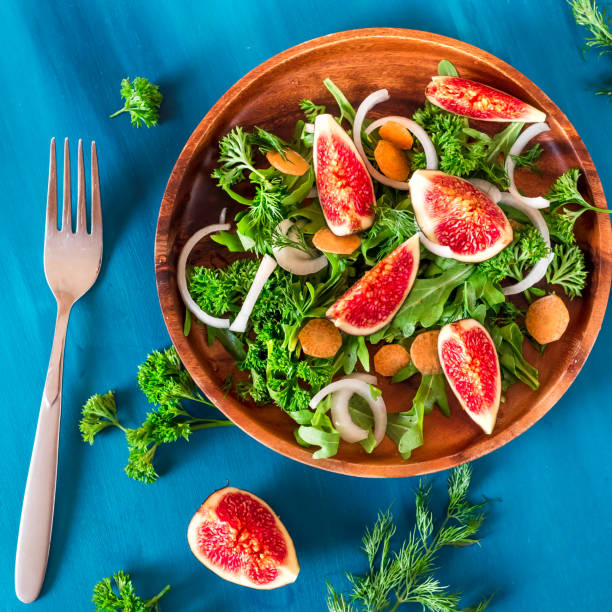 istock Autumn salad of arugula, figs in a brown earthenware plate on a blue background. top view 875253454