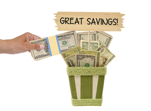 Hand placing one hundred dollar bills in basket filled with money and wood sign Great Savings! on white background