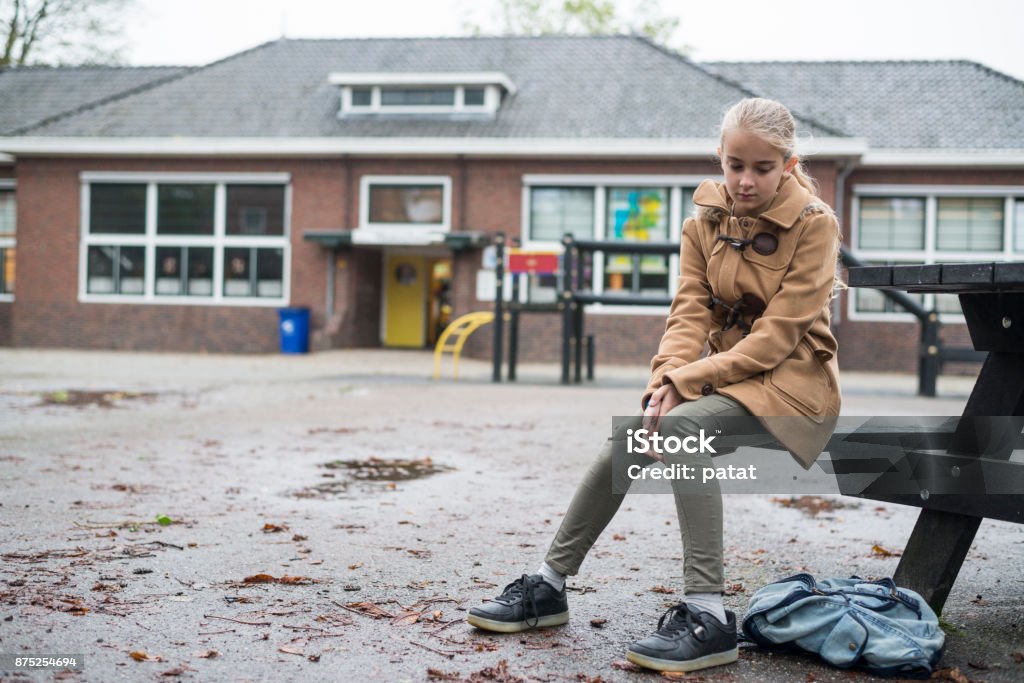 Sad girl sitting at schoolyard Schoolgirl at school outside sad and alone. Concept of bullying or insecurity Child Stock Photo