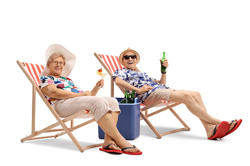 Happy elderly tourists with a cocktail and a bottle of beer seated in deck chairs isolated on white background