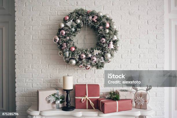 Foto de Uma Tradicional Guirlanda De Natal Brilhante Pendurado Sobre A Lareira Sobre Um Tijolo Branco Parede E Presentes Embalados São Empilhados Em Uma Lareira Com Velas e mais fotos de stock de Natal