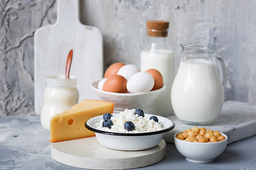 Dairy products on marble table over concrete background. Cheese, farmers cheese, milk, yogurt, sour cream, eggs and smoked cheese. Organic farmers dairy products