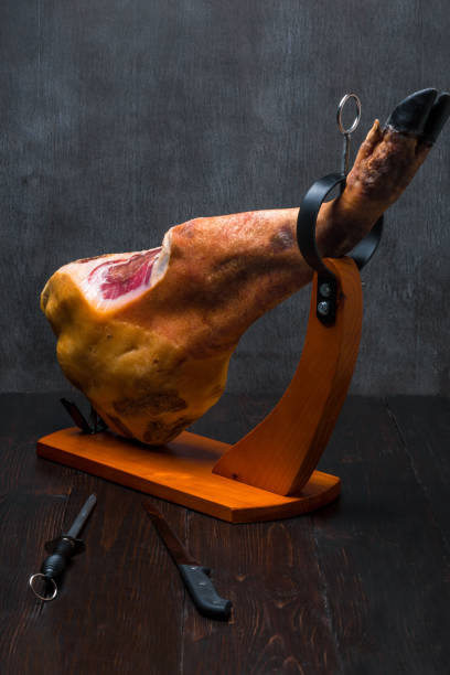 istock Whole mediterranean traditional jamon on a wooden stand with a knife lean on a table. Dark image 875289420
