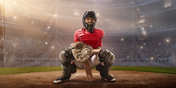 Softball female catcher on a professional arena. Beautiful player in unbranded uniform on big arena. The player waiting to catches the ball and gives signs.