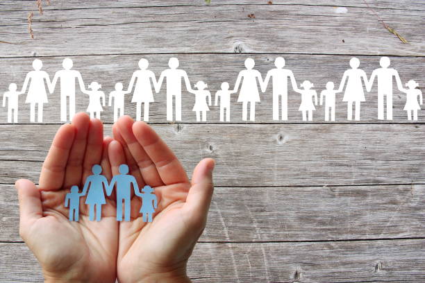 Paper family in hands on wooden background with white families stock photo