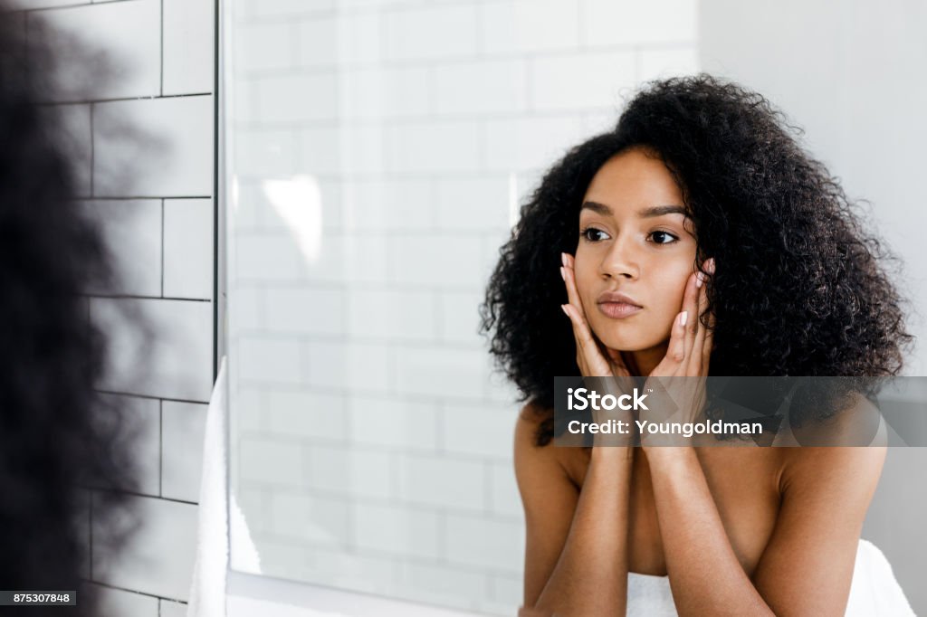 Femme de race mixte masser son visage et en regardant un miroir - Photo de Une seule femme libre de droits