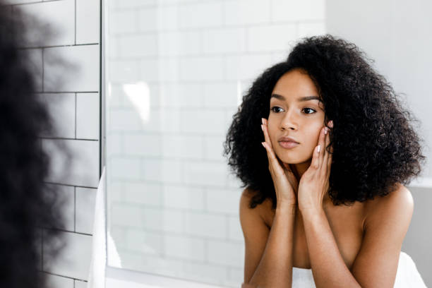 istock Mixed race woman massaging her face and looking at a mirror 875307848